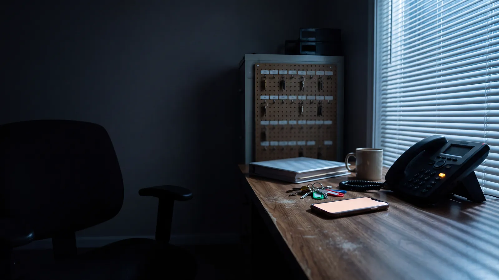 A small property management office after closing, dark except for the streetlight through the window and the glow of the desk phone